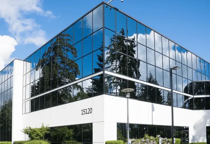 A three story office building with glass walls reflecting trees and sky
