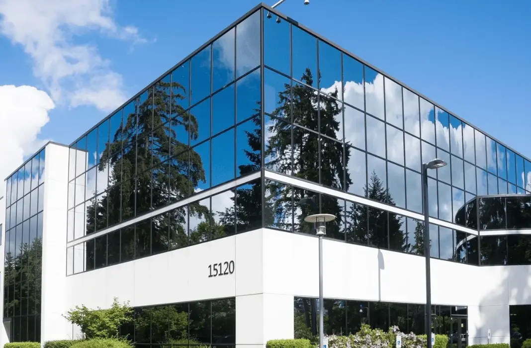 A three story office building with glass walls reflecting trees and sky
