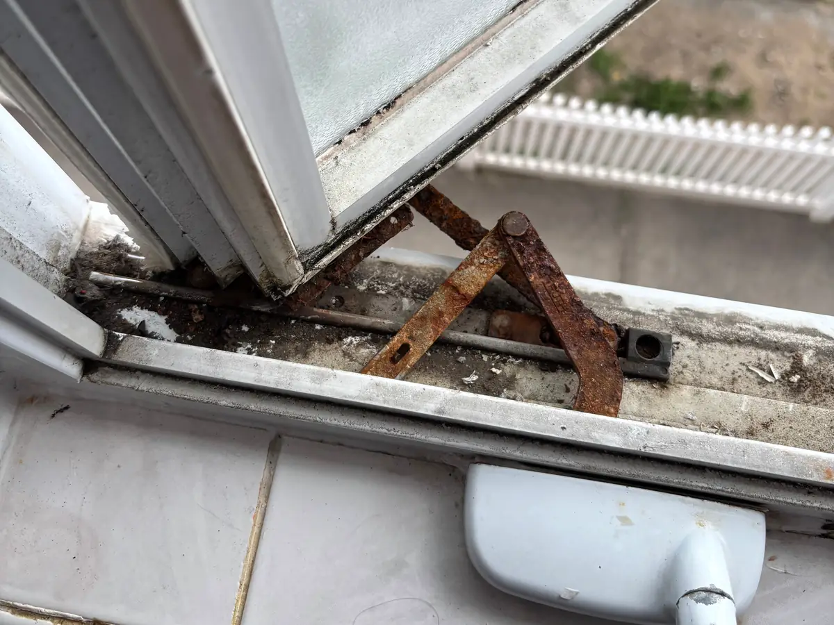 A rusted casement window operator arm in the open window track