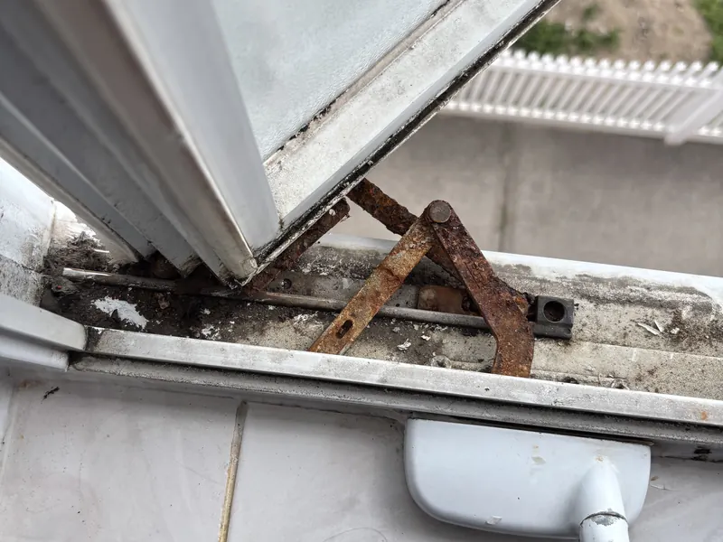 A rusted casement operator arm under an open window sash