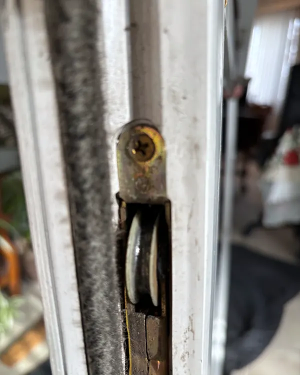A worn sash pulley in an old wood window frame, close up