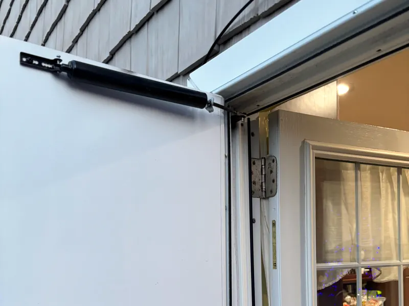 A white storm door held open, its closer arm at the top and a hinge on the frame