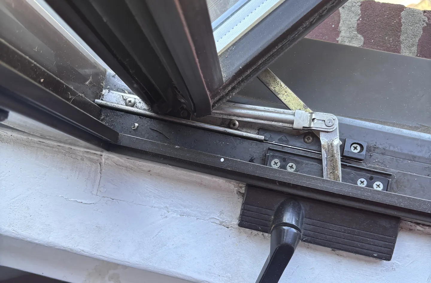 A crank handle and operator arm on a dark casement window