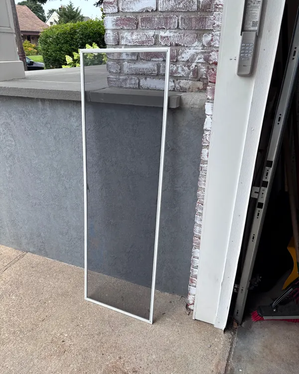 A finished window screen leaning against a wall by a door