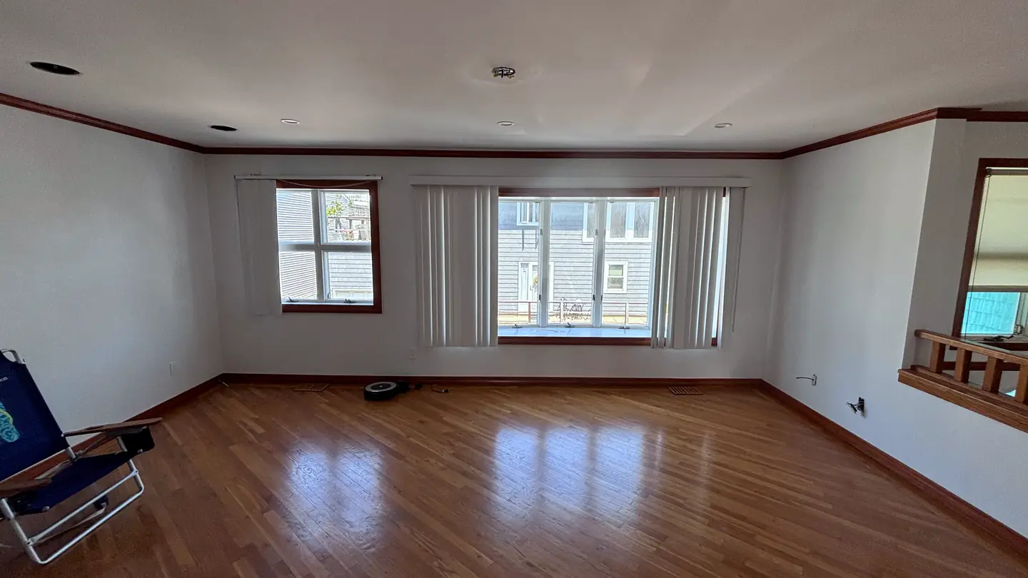 An empty room with hardwood floors and windows on two walls