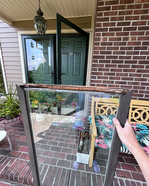 A storm door glass panel held up in front of a brick porch