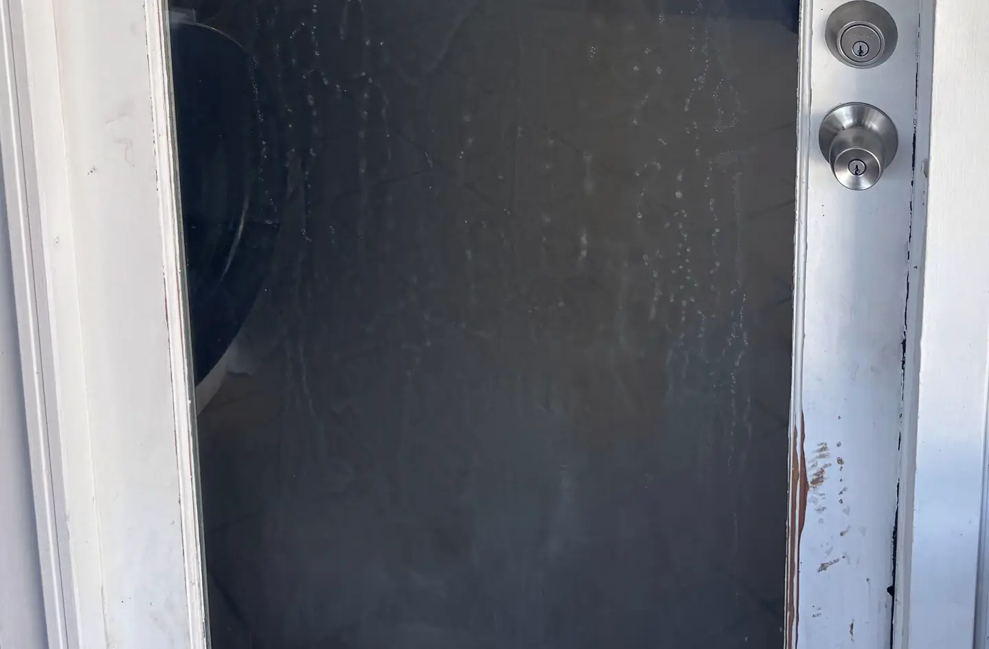 A storm door with a deadbolt and knob on a weathered white frame