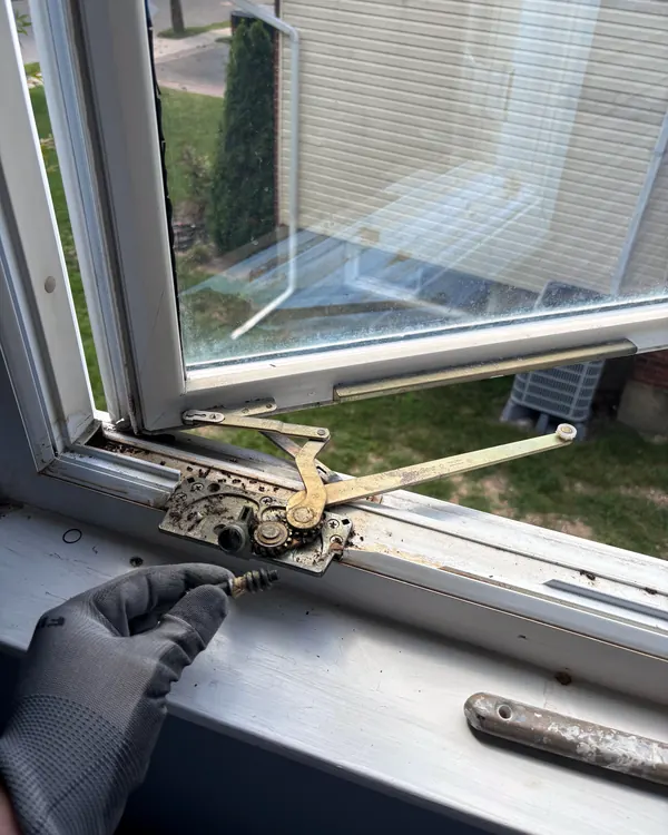 A gloved hand working on a casement window operator on the sill