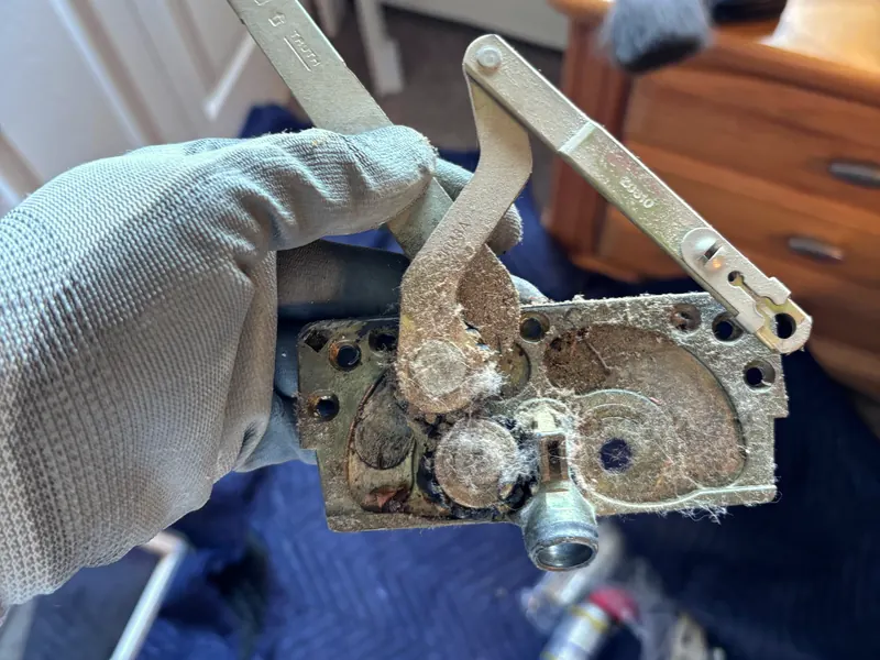 A gloved hand holding a worn casement window operator taken out for rebuild