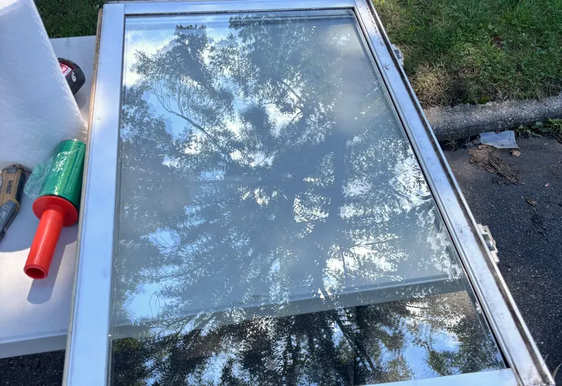 A new insulated glass unit on a work table, with trees reflected in the glass