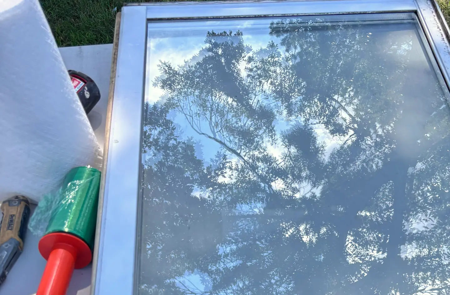 A new insulated glass unit on a work table, with trees reflected in the glass