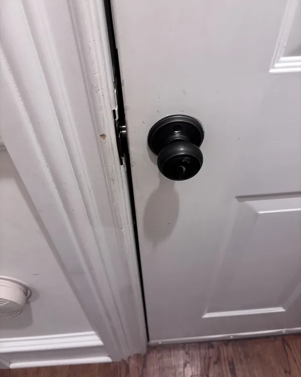 A white panel interior door with a dark knob and an uneven gap at the latch side