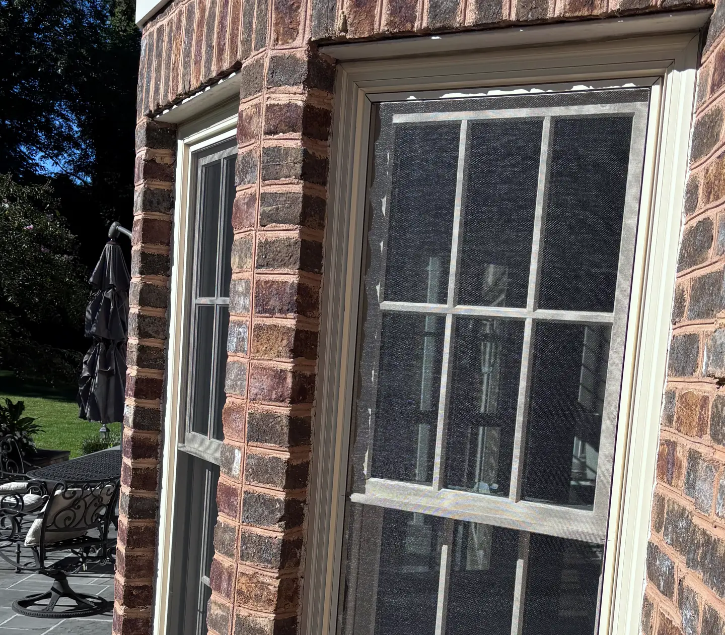 Double hung windows with screens in a brick bay beside a stone patio