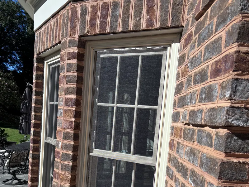 Double hung windows with screens in a brick bay beside a stone patio
