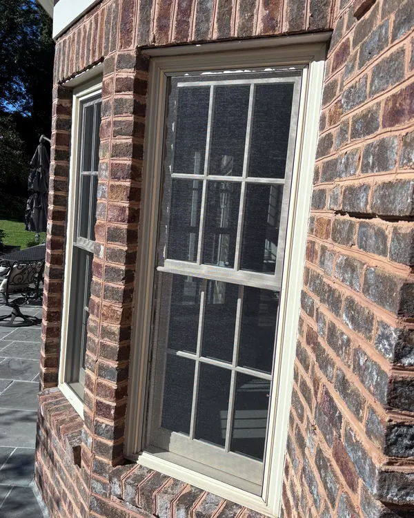 Double hung windows with screens in a brick bay beside a stone patio