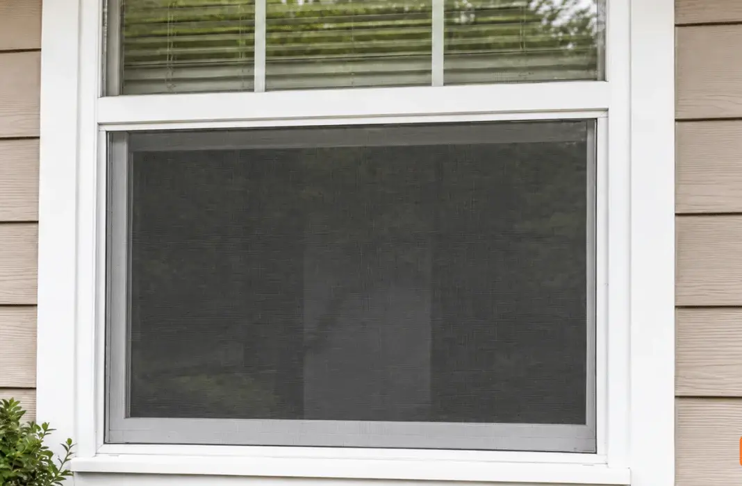 A window screen in a white window frame on tan siding