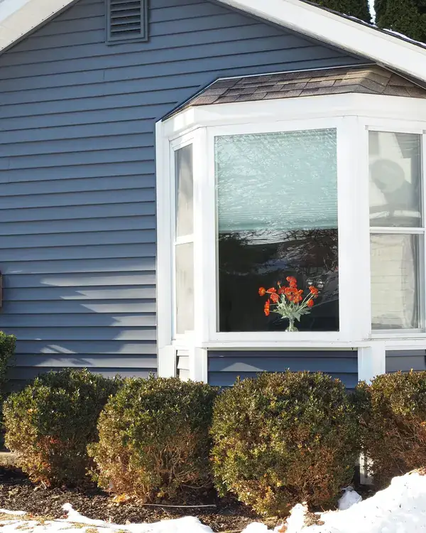 A bay window on the front of a blue sided house
