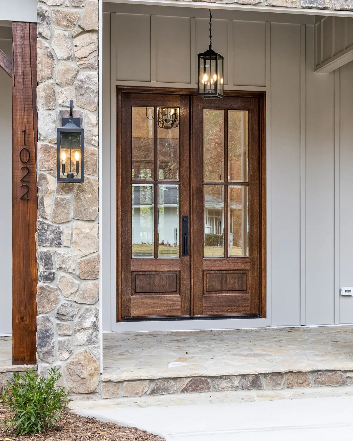 A wood front door with glass panes on the stone porch of a house