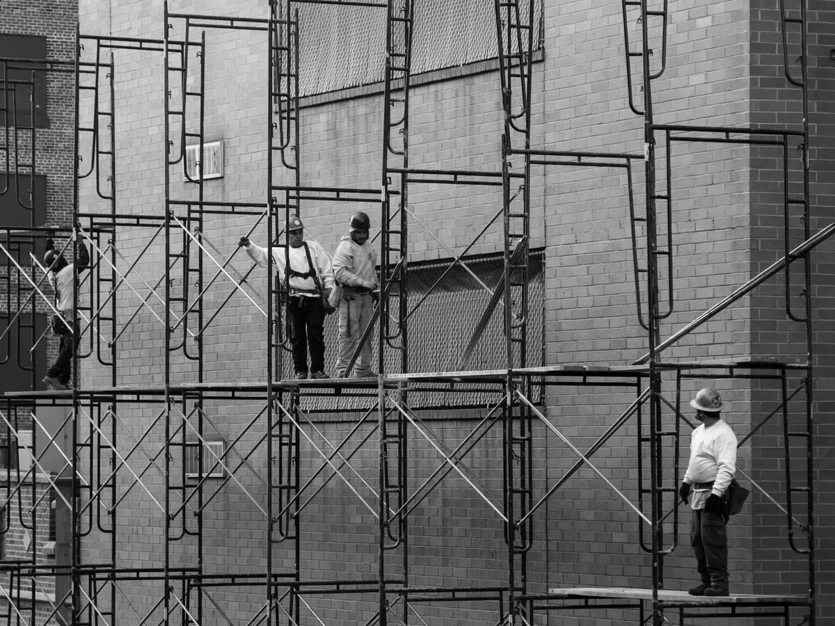 Workers in hard hats and harnesses on scaffolding along a brick building