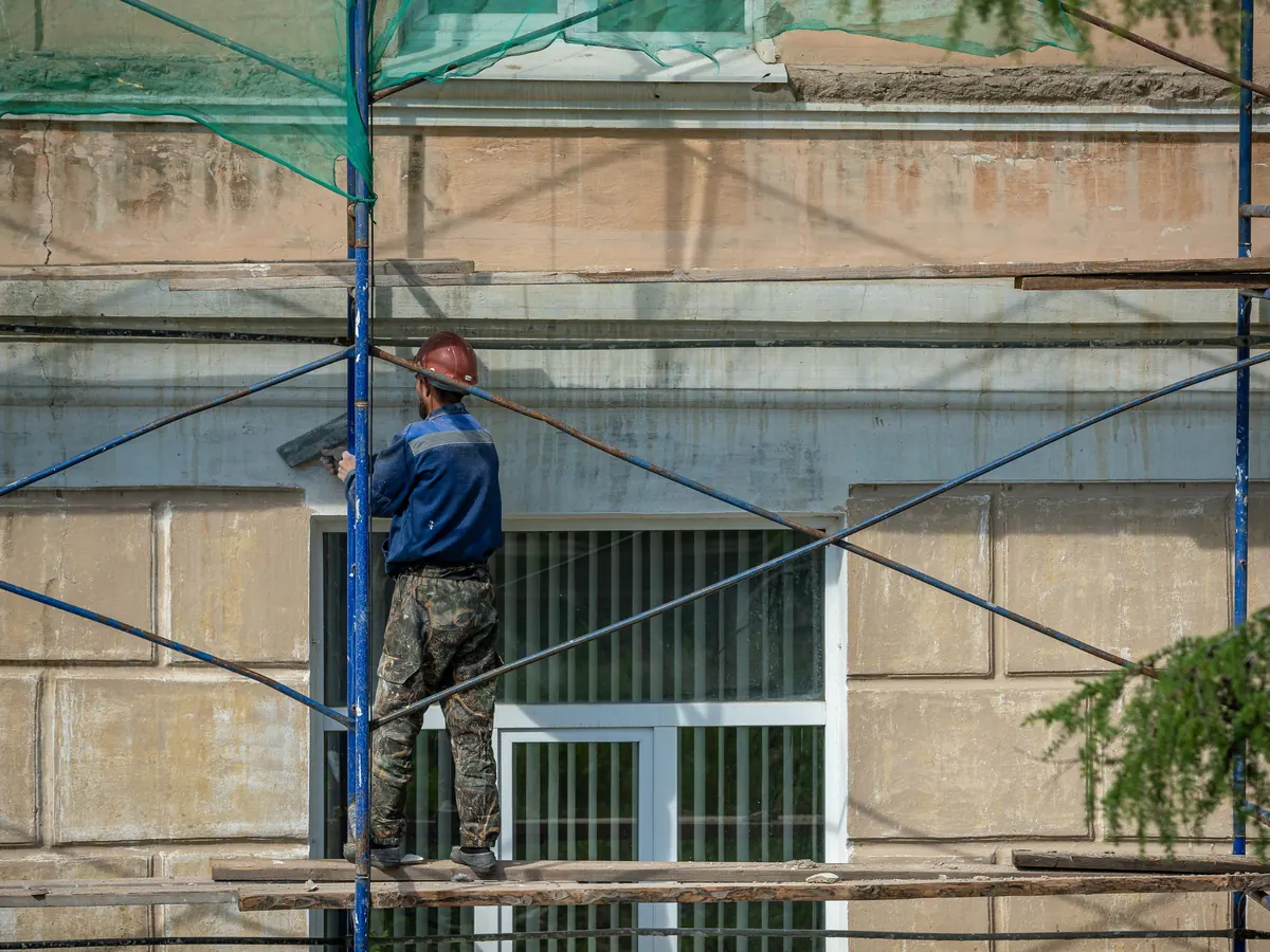 A worker in a hard hat on scaffolding beside a building entrance