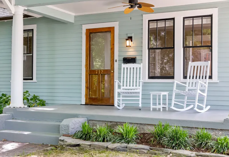 A wood front door with a full glass storm door on the porch of a house
