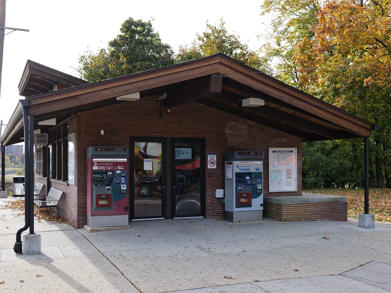 The brick Douglaston train station house with a wide wooden roof among red and gold autumn trees