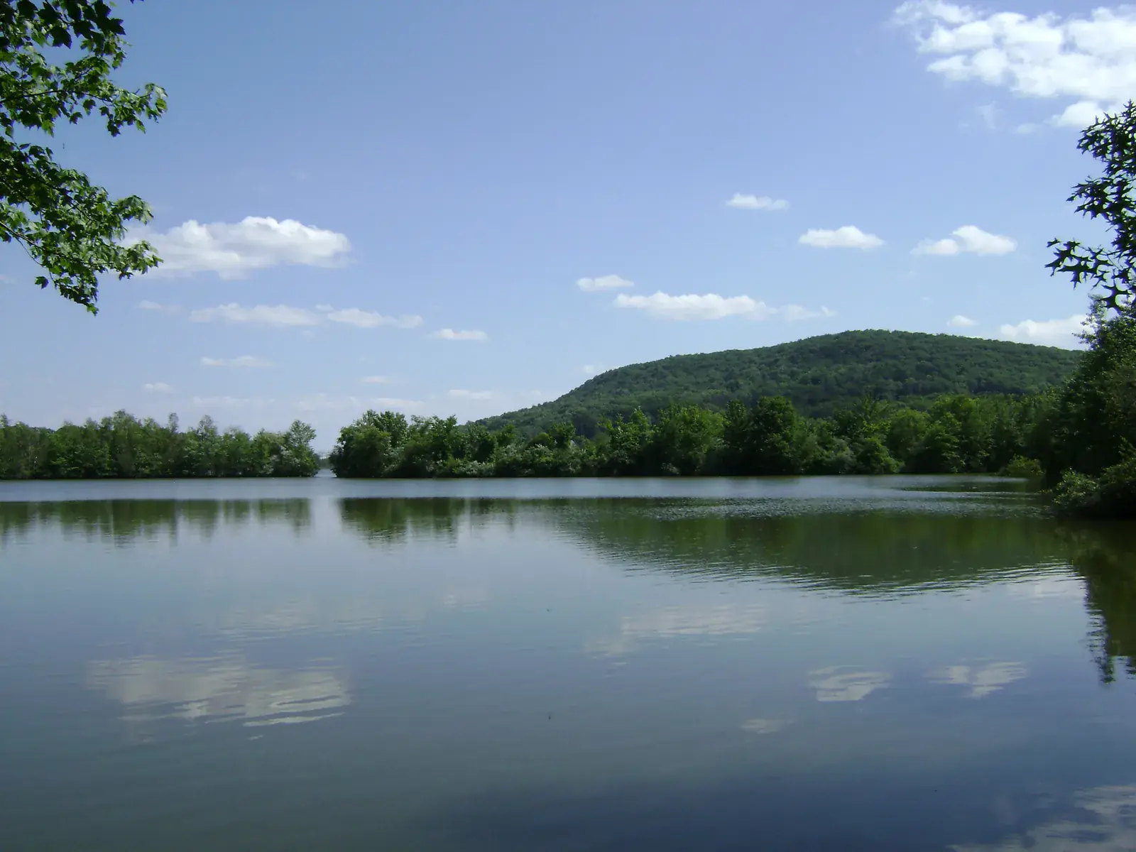 The lake at the Franklin Lakes Nature Preserve with wooded hills beyond under a blue sky with small white clouds