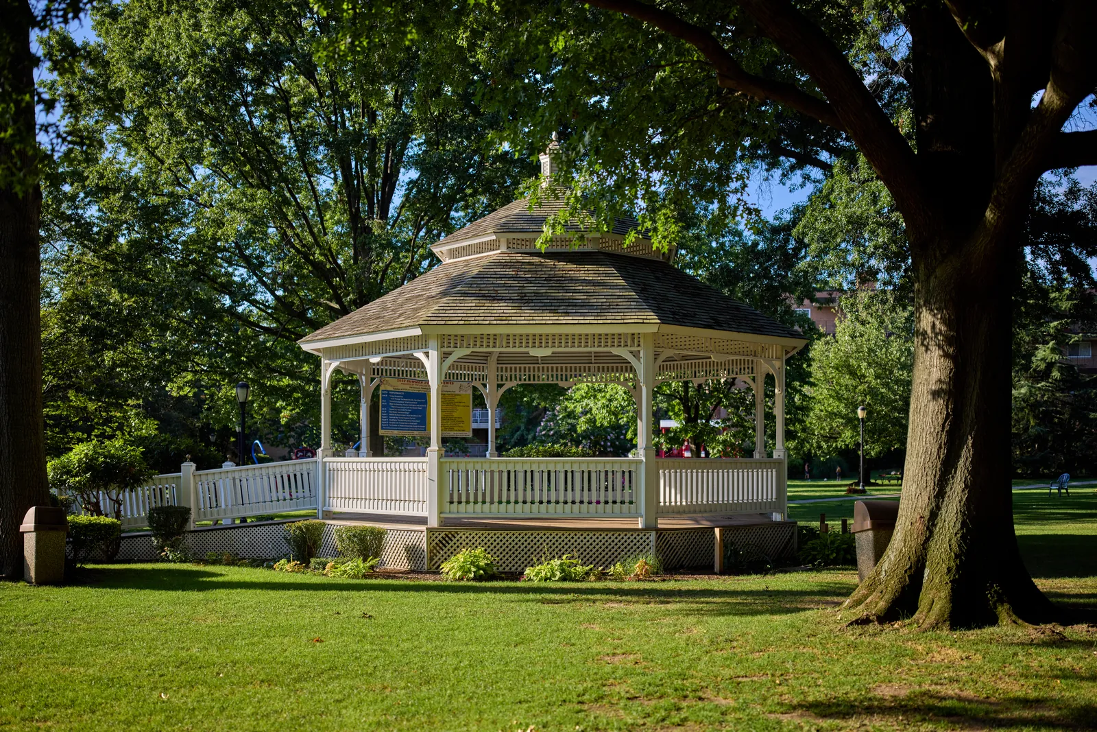 White gazebo under tall shade trees at Firefighters Park in neighboring Great Neck Plaza, NY