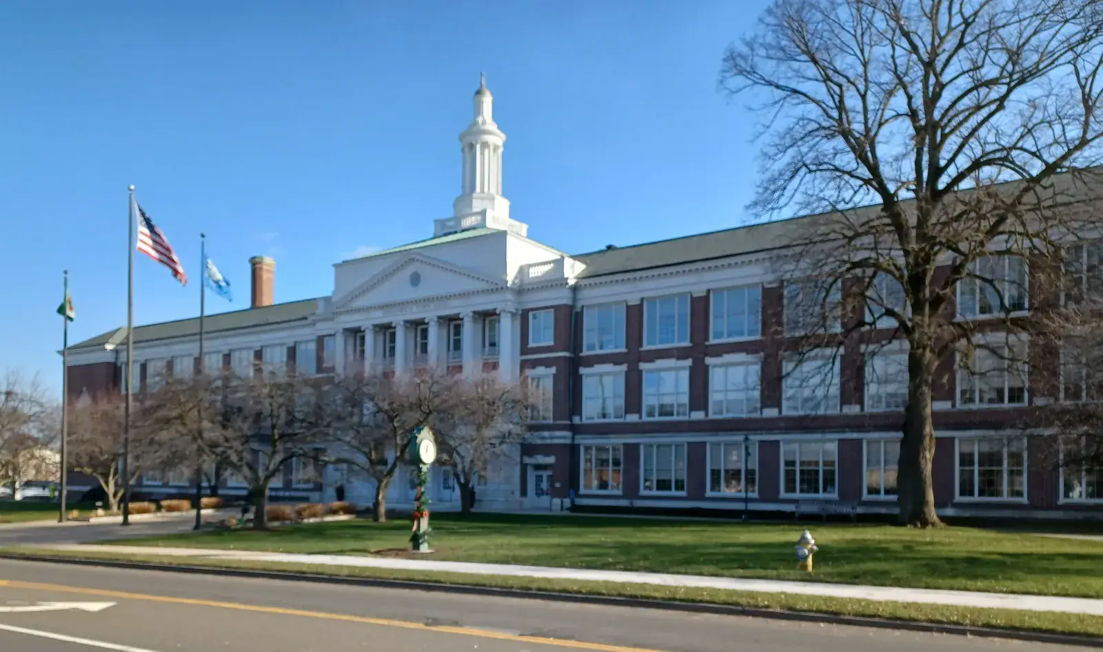 Greenwich Town Hall, a long red-brick building with a white portico and cupola, behind a lawn and bare trees under a clear blue sky