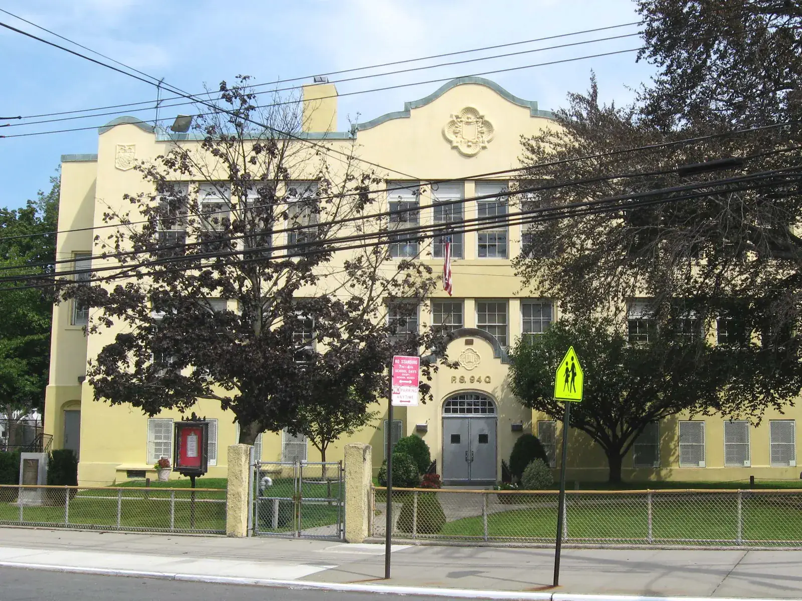 The yellow PS 94 school building on Little Neck Parkway with its curved parapet behind a lawn under a blue sky
