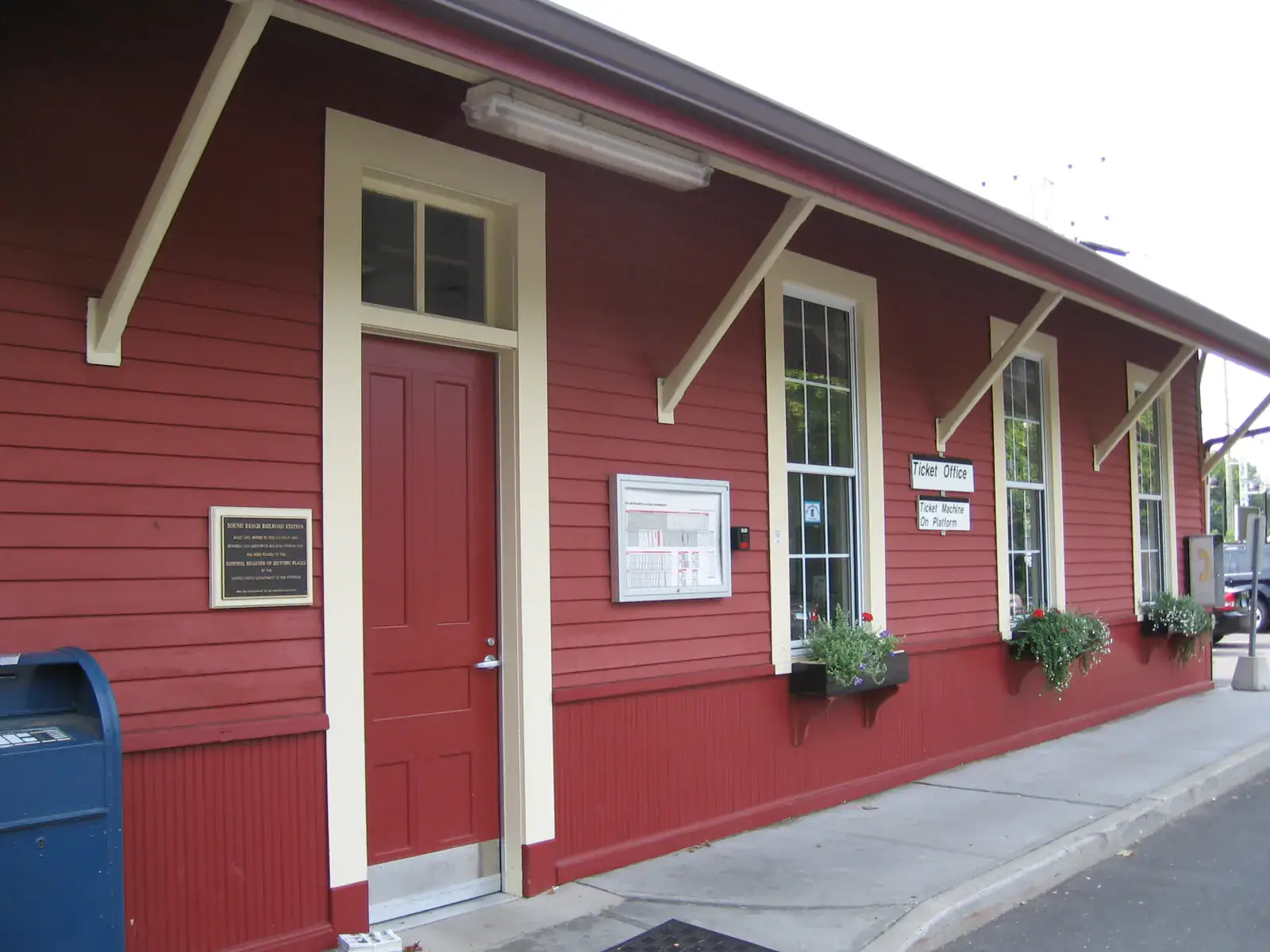 The red clapboard Old Greenwich train station house with cream trim and flower boxes under its windows