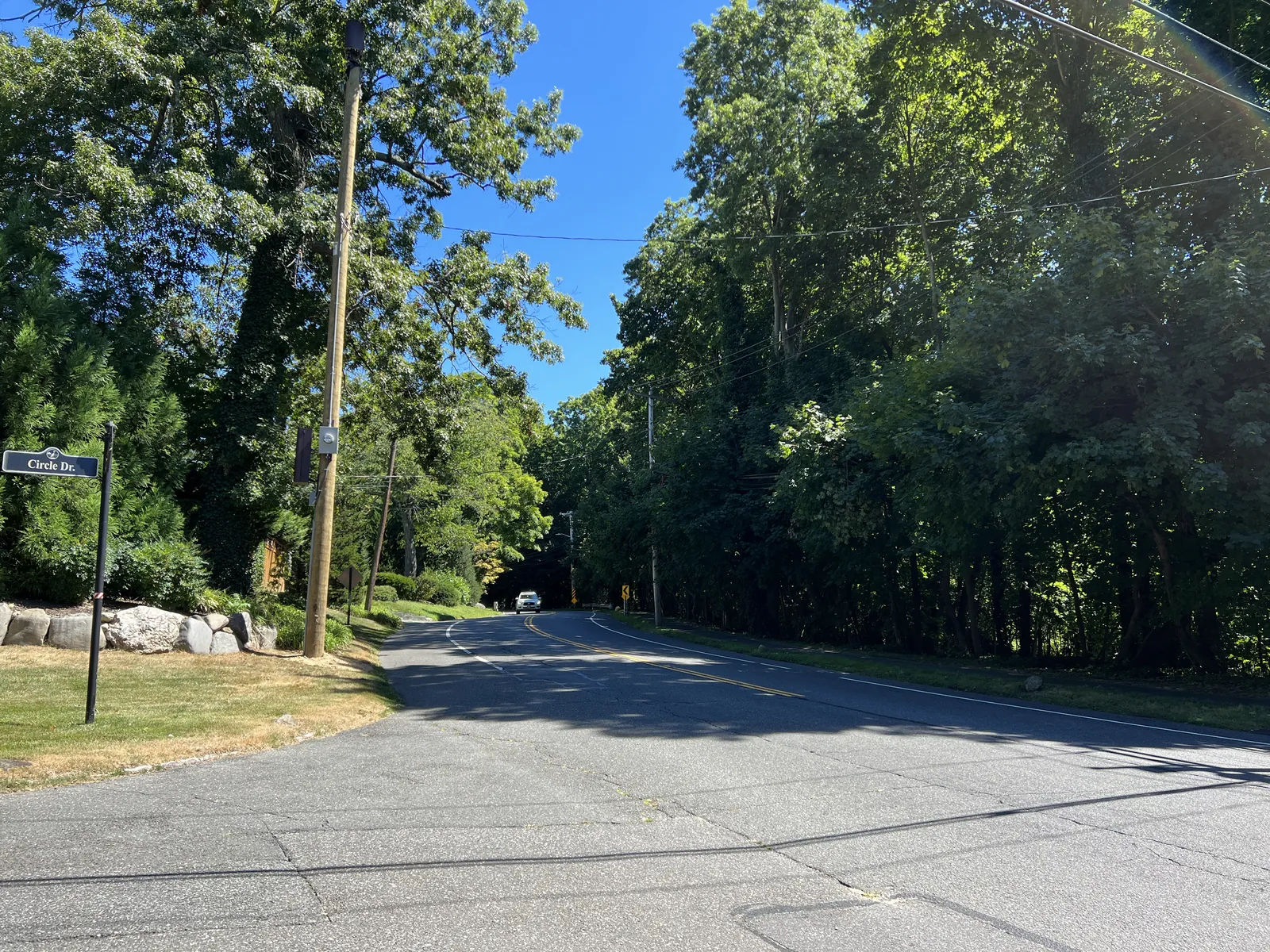 Wooded Stonytown Road at Circle Drive under a blue summer sky in Plandome Manor, NY