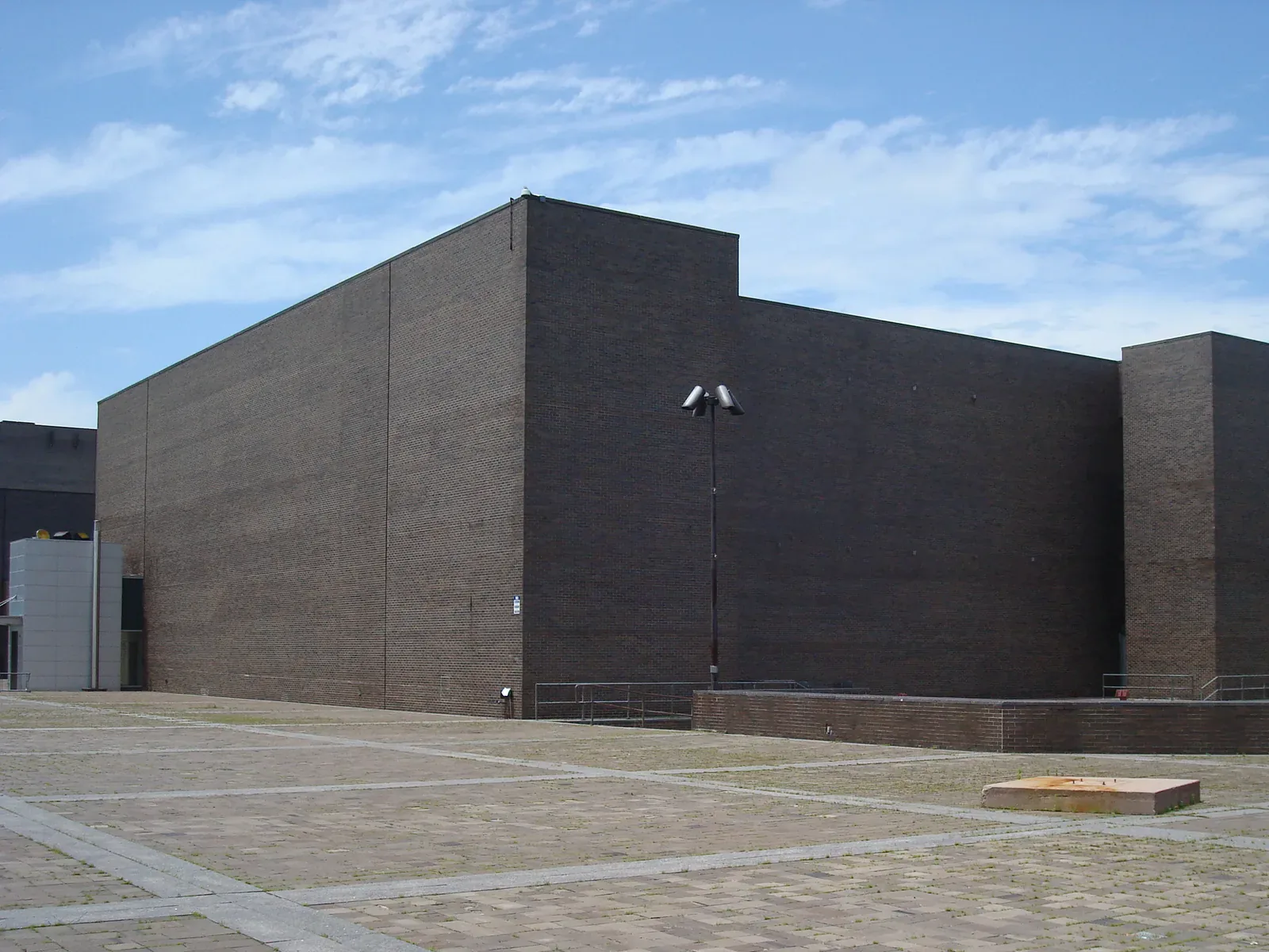 The dark brick Performing Arts Center on the plaza of the SUNY Purchase campus under a blue sky with white clouds