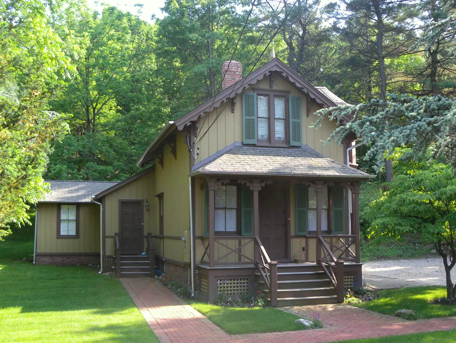 Small yellow cottage with vertical board siding, green shutters and a front porch, Eastman Cottage in neighboring Roslyn, NY