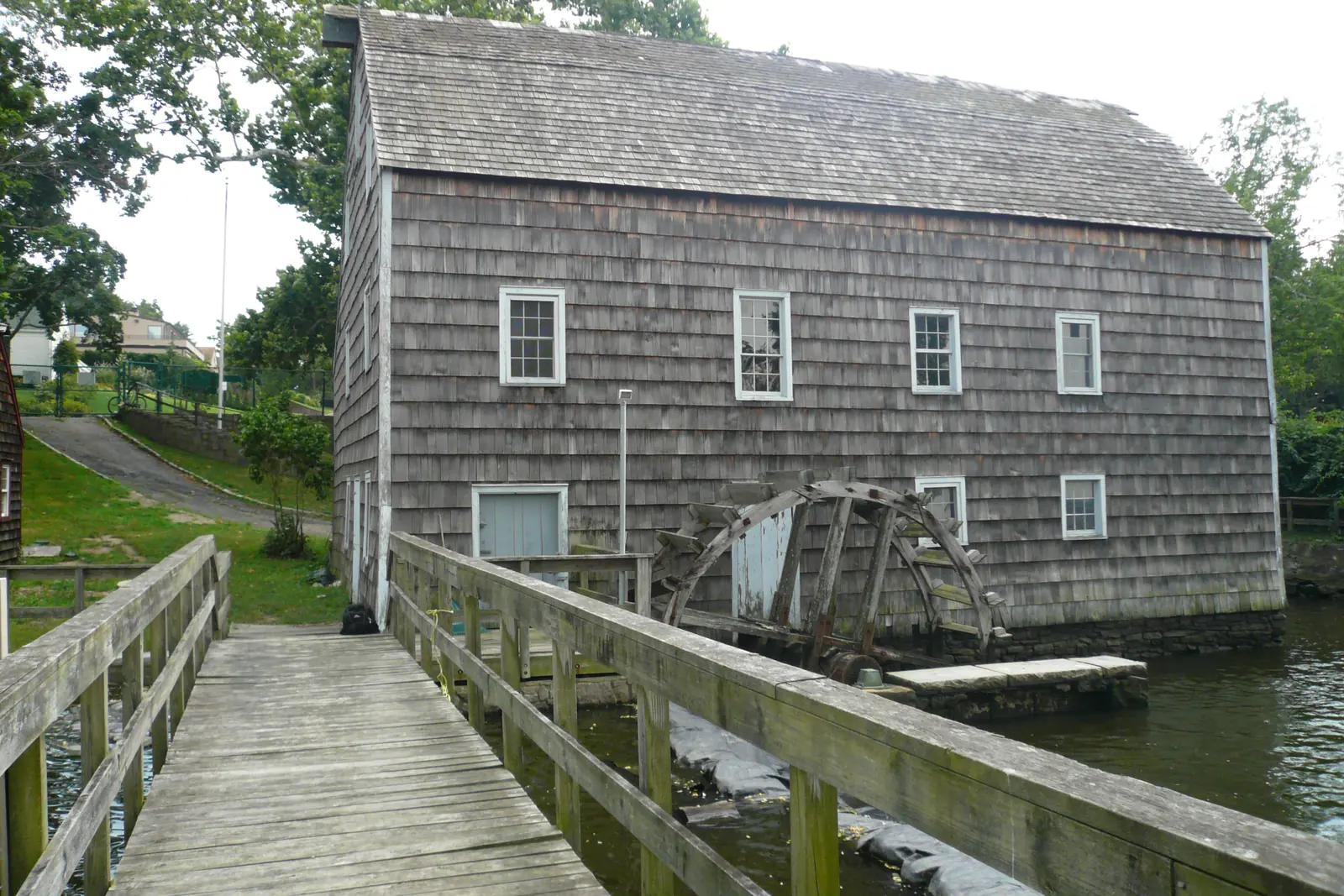 Saddle Rock Grist Mill, a shingled mill with a wooden water wheel on Little Neck Bay, seen from its boardwalk in Saddle Rock, NY